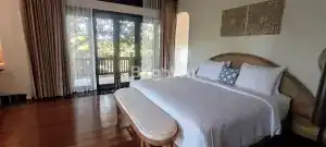 Bedroom with large glass doors opening to balcony and lush greenery.