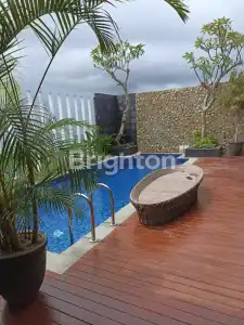 Poolside view of a modern villa with lush greenery and wooden deck in Kedungu.